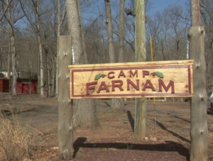 Wooden sign that reads" Camp Farnam" with trees in the background